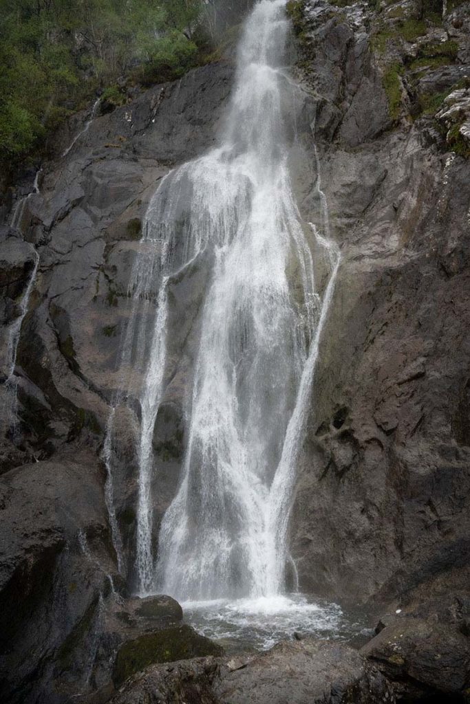 Rushing Aber Falls waterfall pouring down over the grey rockface into a pool below. 