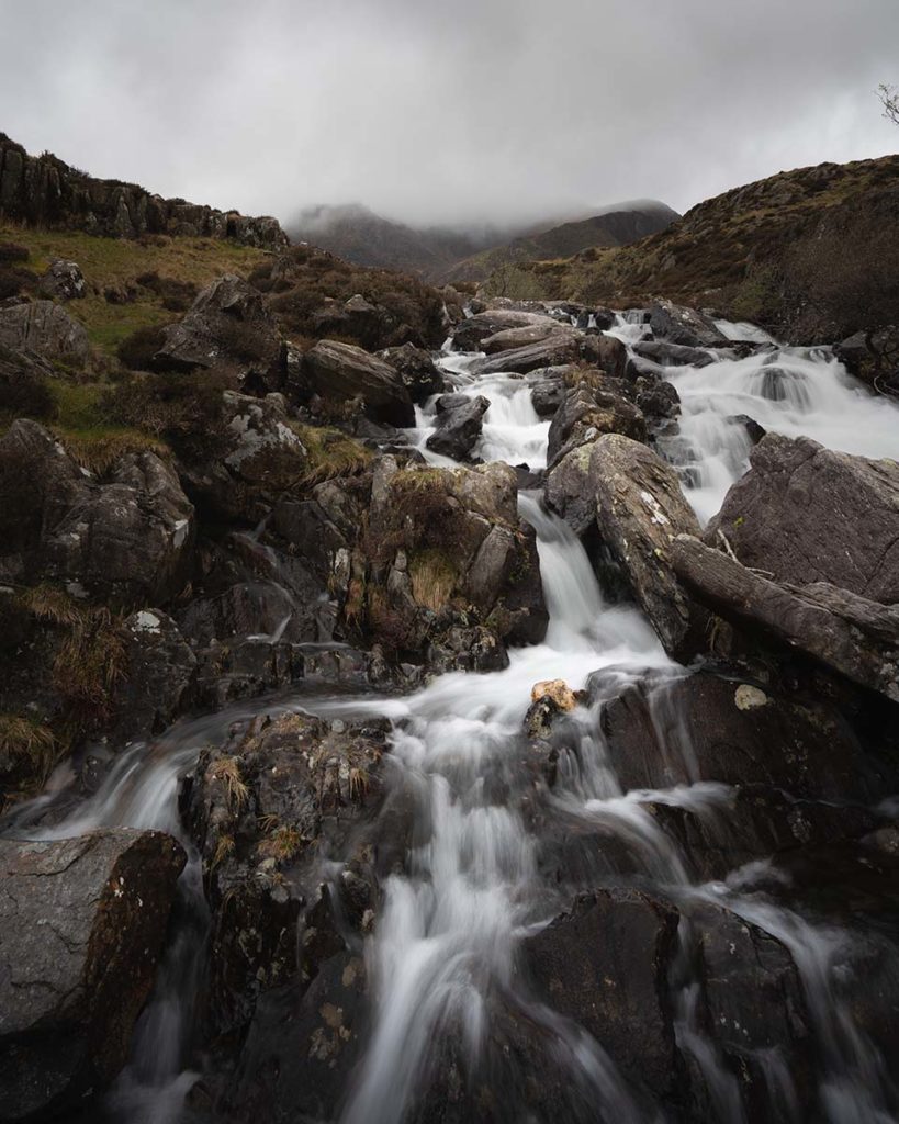 Small Rushing waterfall over craggy grey rocks with a foggy backdrop in Cwm Idwal
