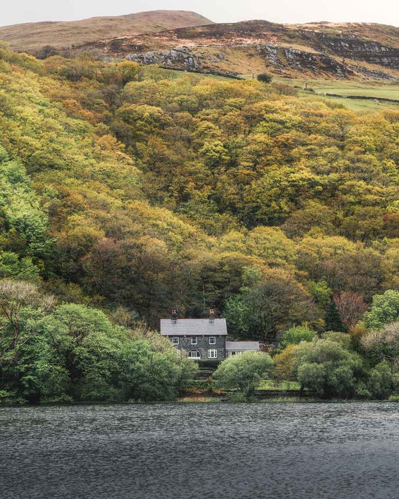 Quaint cottage surrounded by autumnal looking trees on the banks of  alake