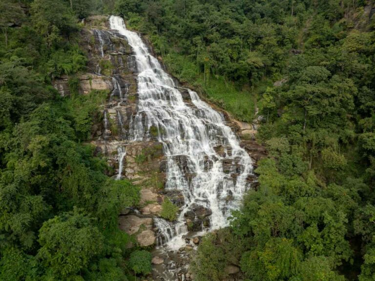 A stunning aerial shot of Mae Ya Waterfall surrounded by dense greenery, highlighting the waterfall’s grandeur and seamless integration into the natural forested landscape. Taken with a drone.