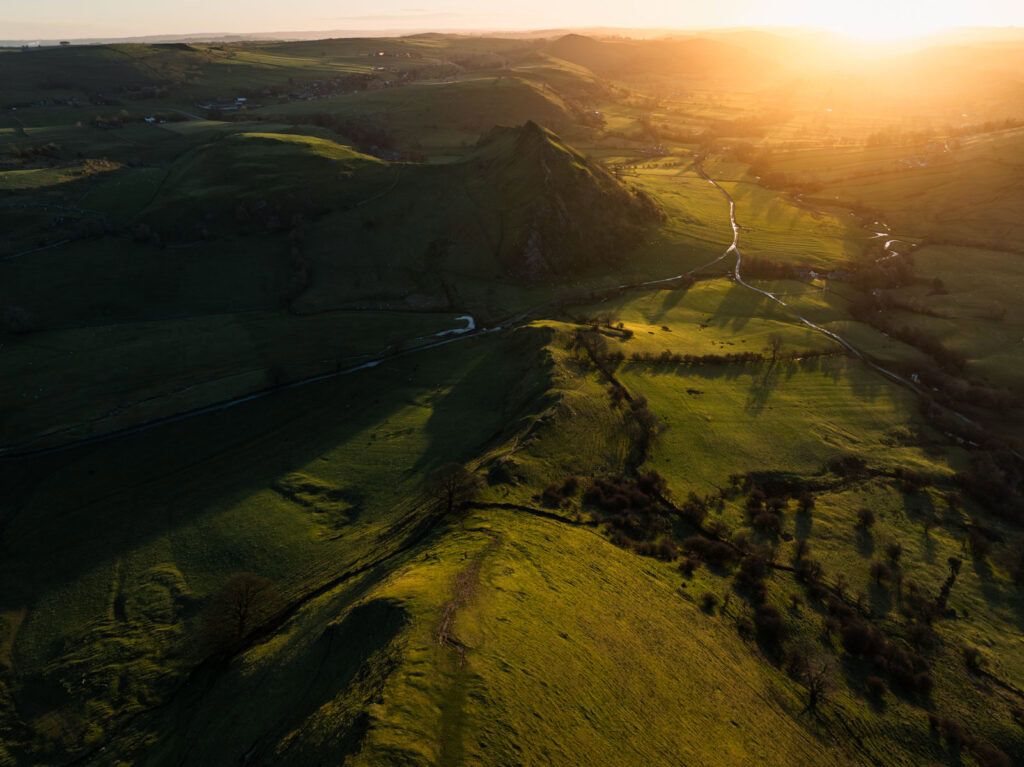 Golden evening light casting long shadows across rolling green hills and winding valleys.