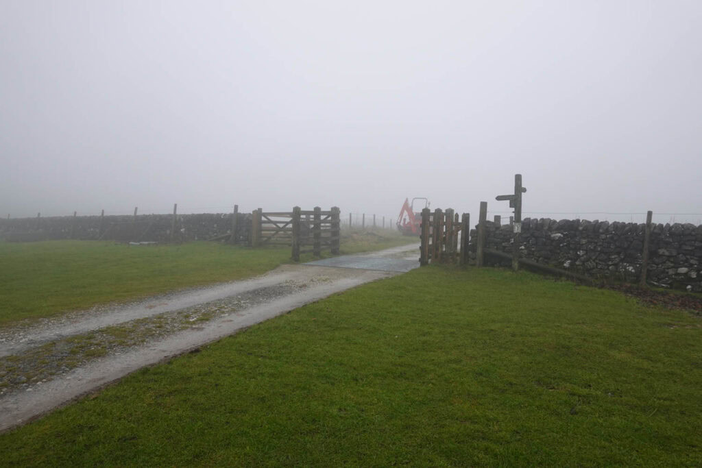 Farm track and gate beside a stone wall, marking a point where walkers should continue straight rather than passing through.